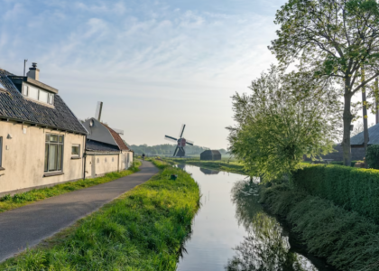 water canal at the side of a narrow road with a windmill on a field